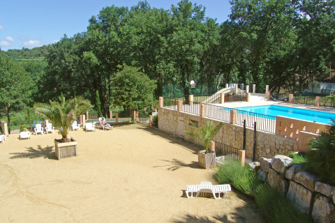 En solrig udendørs pool og sandområde omgivet af grønne træer i Slow Village Provence Occitane, Occitanie.