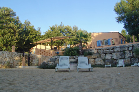 Tumbonas sobre arena frente a un muro de piedra y casas de vacaciones en Slow Village Provence Occitane, Occitanie, Francia.