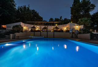 Piscine éclairée en soirée devant le bâtiment principal au Slow Village Provence Occitane en Occitanie, France.
