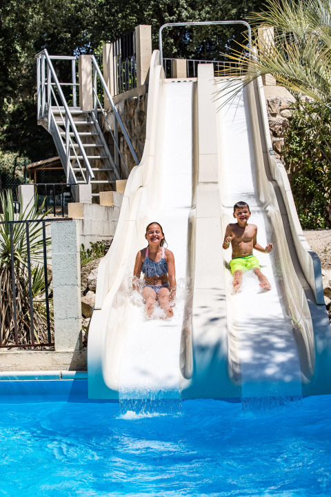 Twee kinderen glijden van waterglijbanen in het zwembad bij Slow Village Provence Occitane, Occitanië, Frankrijk.