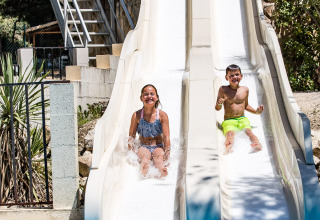 Twee kinderen glijden van waterglijbanen in het zwembad bij Slow Village Provence Occitane, Occitanië, Frankrijk.