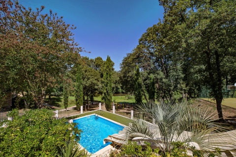 Vista de una piscina y vegetación exuberante rodeadas de árboles en Slow Village Provence Occitane, Occitania, Francia.