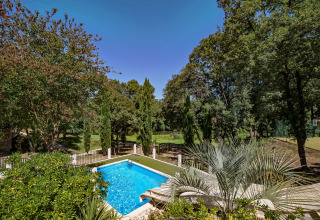 Udsigt over swimmingpool og frodig have omkranset af træer i Slow Village Provence Occitane, Occitanie, Frankrig.