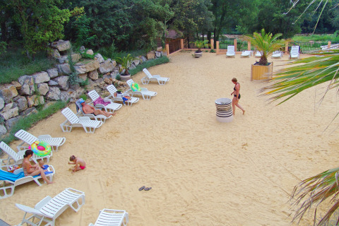 Zona de arena clara con hamacas y visitantes descansando en Slow Village Provence Occitane, Occitania, Francia.