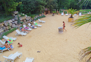 Solrig sandstrand med liggestole og gæster i afslappet stemning på Slow Village Provence Occitane, Frankrig.