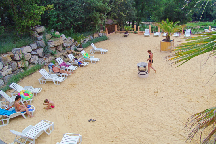 Sunny sandy area with lounge chairs and people relaxing at Slow Village Provence Occitane in Occitanie, France.