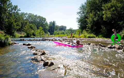 Kids play with inflatables in a shallow river at Slow Village Provence Occitane holiday park in Occitanie, France.