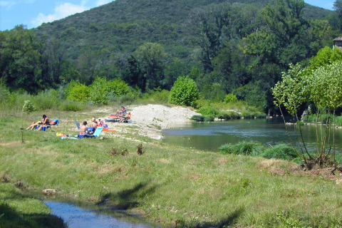 Gezinnen zonnebaden en ontspannen bij een rustige rivier tussen groene heuvels in Occitanie, Frankrijk.