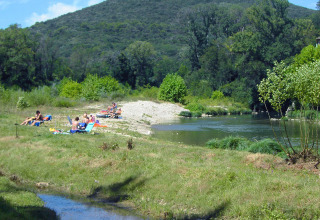 Gezinnen zonnebaden en ontspannen bij een rustige rivier tussen groene heuvels in Occitanie, Frankrijk.