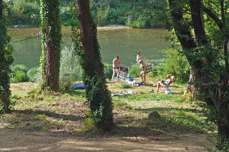People relax by the river at Slow Village Provence Occitane holiday park in Occitanie, France.