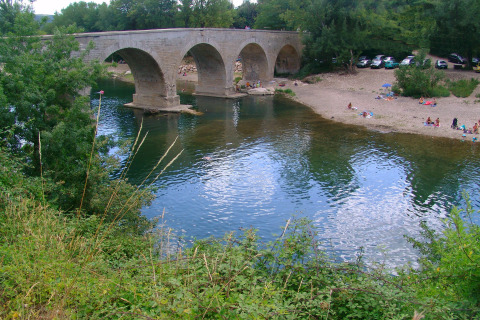 Stenen brug over een rivier bij Slow Village Provence Occitane, mensen op het strand en geparkeerde auto's.