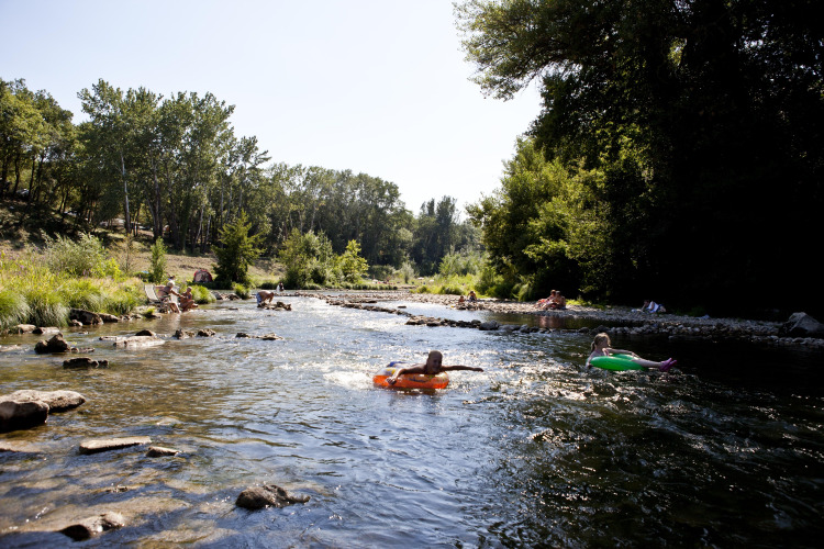 People relax and float on inflatable tubes in a shallow river at Slow Village Provence Occitane, France.