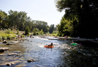 People relax and float on inflatable tubes in a shallow river at Slow Village Provence Occitane, France.