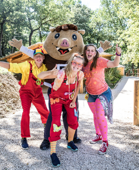 Vier vrolijke mensen en een mascotte poseren buiten in kleurrijke outfits bij Slow Village Provence Occitane.