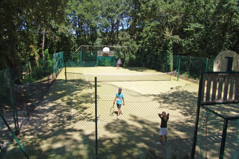 Cancha de tenis rodeada de árboles con personas jugando en Slow Village Provence Occitane, Francia.