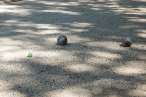 Bolas de petanca y un boliche verde en una cancha sombreada en Slow Village Provence Occitane, Occitania, Francia.