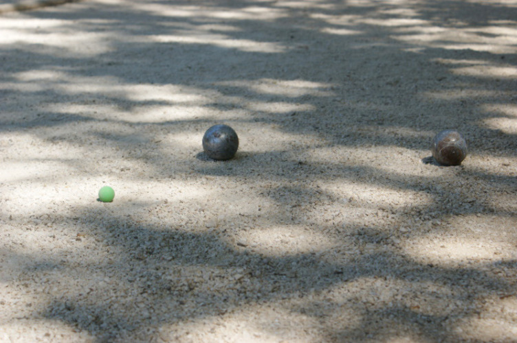 Petanque balls and a green jack on a shaded sandy court at Slow Village Provence Occitane, Occitanie, France.