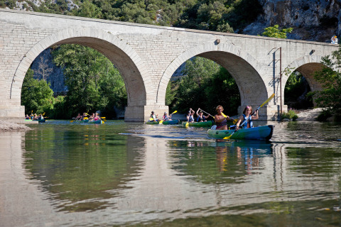 People kayaking under an old stone bridge at Slow Village Provence Occitane holiday park in Occitanie, France.