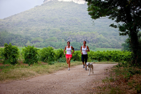 Dos mujeres corren con un perro por un sendero entre viñedos en Slow Village Provence Occitane, Occitania, Francia.