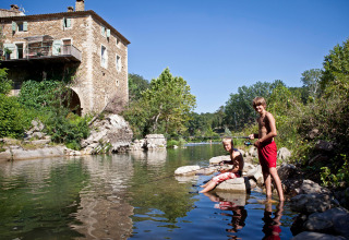 Due bambini pescano vicino a un fiume di fronte a una casa in pietra a Slow Village Provence Occitane, Francia.