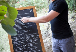 Man leest buiten een menubord bij Slow Village Provence Occitane vakantiedorp in Occitanië, Frankrijk.