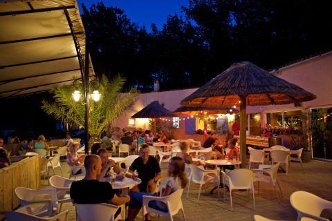 Escena nocturna en la terraza del Slow Village Provence Occitane, Francia, personas disfrutan bajo sombrillas de paja.