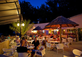 Buitenrestaurant bij Slow Village Provence Occitane, Frankrijk, mensen genieten ‘s avonds onder rieten parasols.