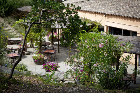 Terrasse extérieure avec tables rondes, fleurs et verdure à Slow Village Provence Occitane, Occitanie.