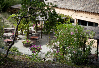 Terrasse extérieure avec tables rondes, fleurs et verdure à Slow Village Provence Occitane, Occitanie.