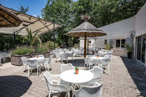 Buitenterras met witte tafels, stoelen, rieten parasols en planten in Slow Village Provence Occitane, Frankrijk.