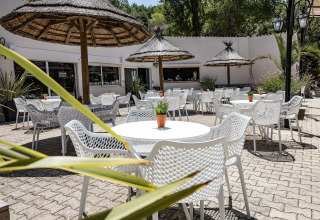 Buitenterras met witte stoelen, ronde tafels en rieten parasols bij Slow Village Provence Occitane, Frankrijk.