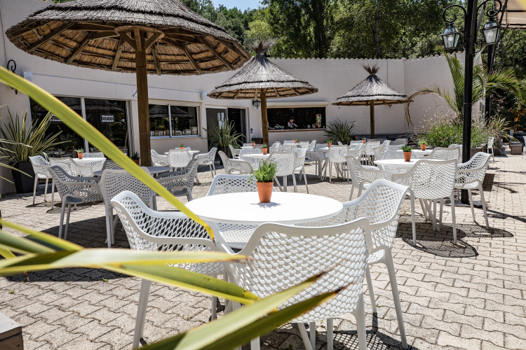 Outdoor dining area with white chairs, round tables and straw umbrellas at Slow Village Provence Occitane, France.