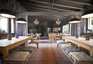 Rustiek restaurant in Slow Village Provence Occitane met houten tafels, zitkussens en sfeervolle kroonluchters.