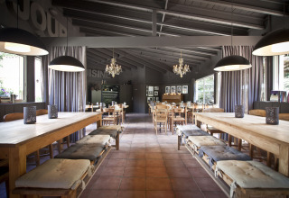 Sala da pranzo rustica a Slow Village Provence Occitane con tavoli in legno, cuscini e lampadari pendenti.