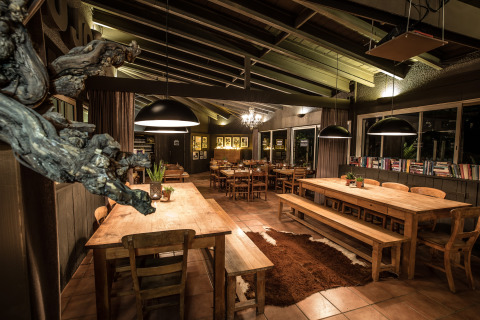 Gezellige eetplek met houten tafels, banken, grote lampen en boeken in Slow Village Provence Occitane, Frankrijk.