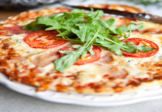 Primo piano di una pizza con pomodoro fresco, mozzarella e rucola su un piatto bianco in Occitanie, Francia.