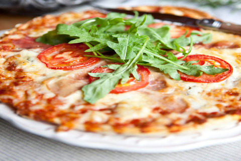 Close-up of a pizza topped with fresh tomato slices, mozzarella, and arugula on a white plate in Occitanie.