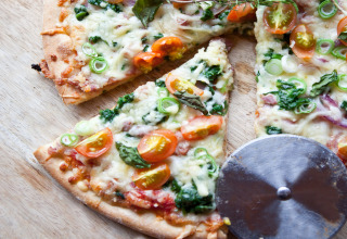 Pizza appena sfornata con pomodorini, spinaci e cipollotti, tagliata a fette su un piano di legno.