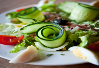 Nærbillede af en frisk salat med agurk, tomat, æg og grønne blade, serveret på en hvid tallerken.