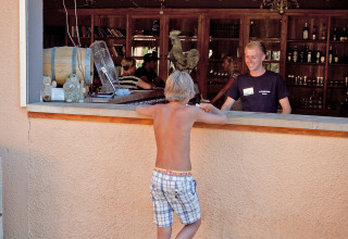 Een jongen zonder hemd bestelt aan een buitenbar bij Slow Village Provence Occitane in Occitanië, Frankrijk.