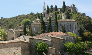 Vista del pintoresco pueblo La Roque-sur-Cèze en Occitania, Francia, con casas de piedra y vegetación en la colina.