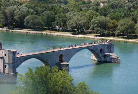 Imagen de un puente de piedra sobre un río cerca de La Roque-sur-Cèze, rodeado de abundante vegetación.