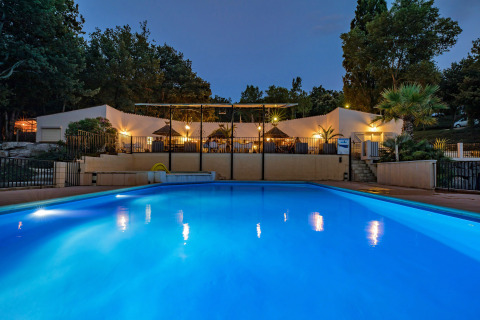 Illuminated swimming pool at night at Slow Village Provence Occitane holiday park in Occitanie, France.