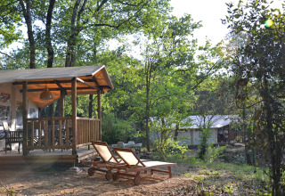 Safaritent en houten ligstoelen bij Slow Village Provence Occitane, gelegen in een groen boslandschap.