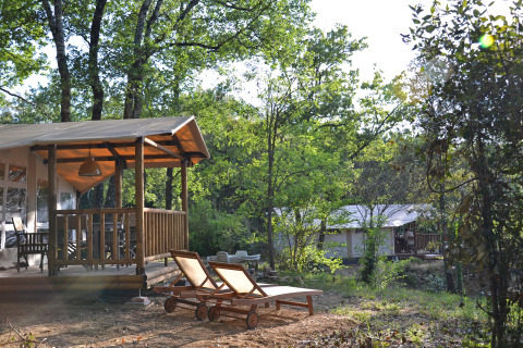 Safari tent lodge and wooden sun loungers at Slow Village Provence Occitane, nestled in a lush forest.