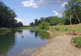 Folk nyder afslapning ved en flodbred på Slow Village Provence Occitane feriepark i Occitanie, Frankrig.