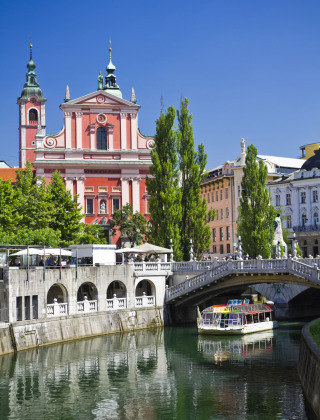 Foto de una iglesia colorida y un barco en el río en Ljubljana, Eslovenia, bajo un cielo azul claro.