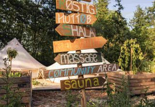 Hand-painted wooden signpost at RØSTIG holiday park, Utrecht, Netherlands, surrounded by green nature.