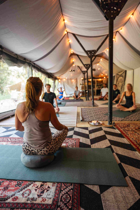 Personas en una clase de yoga bajo una carpa con alfombras y luces en el parque vacacional RØSTIG, Utrecht, Países Bajos.