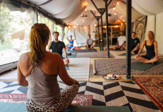 Mensen doen yoga onder een tent met tapijten en sfeerverlichting in vakantiepark RØSTIG te Utrecht, Nederland.